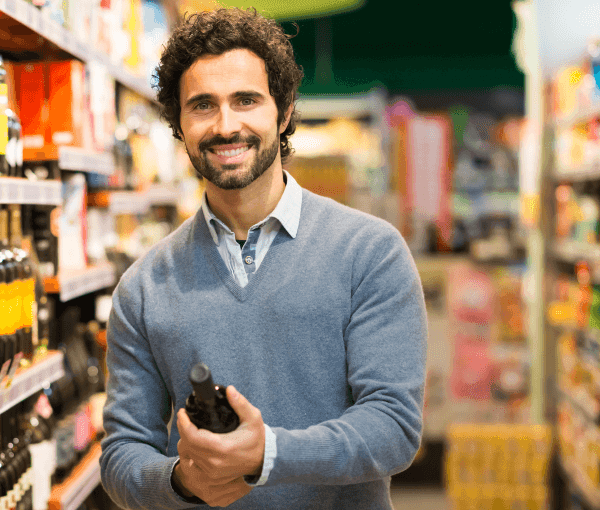 A man holding a wine bottle smiling because he has Wine Shop Workers' Compensation Insurance.